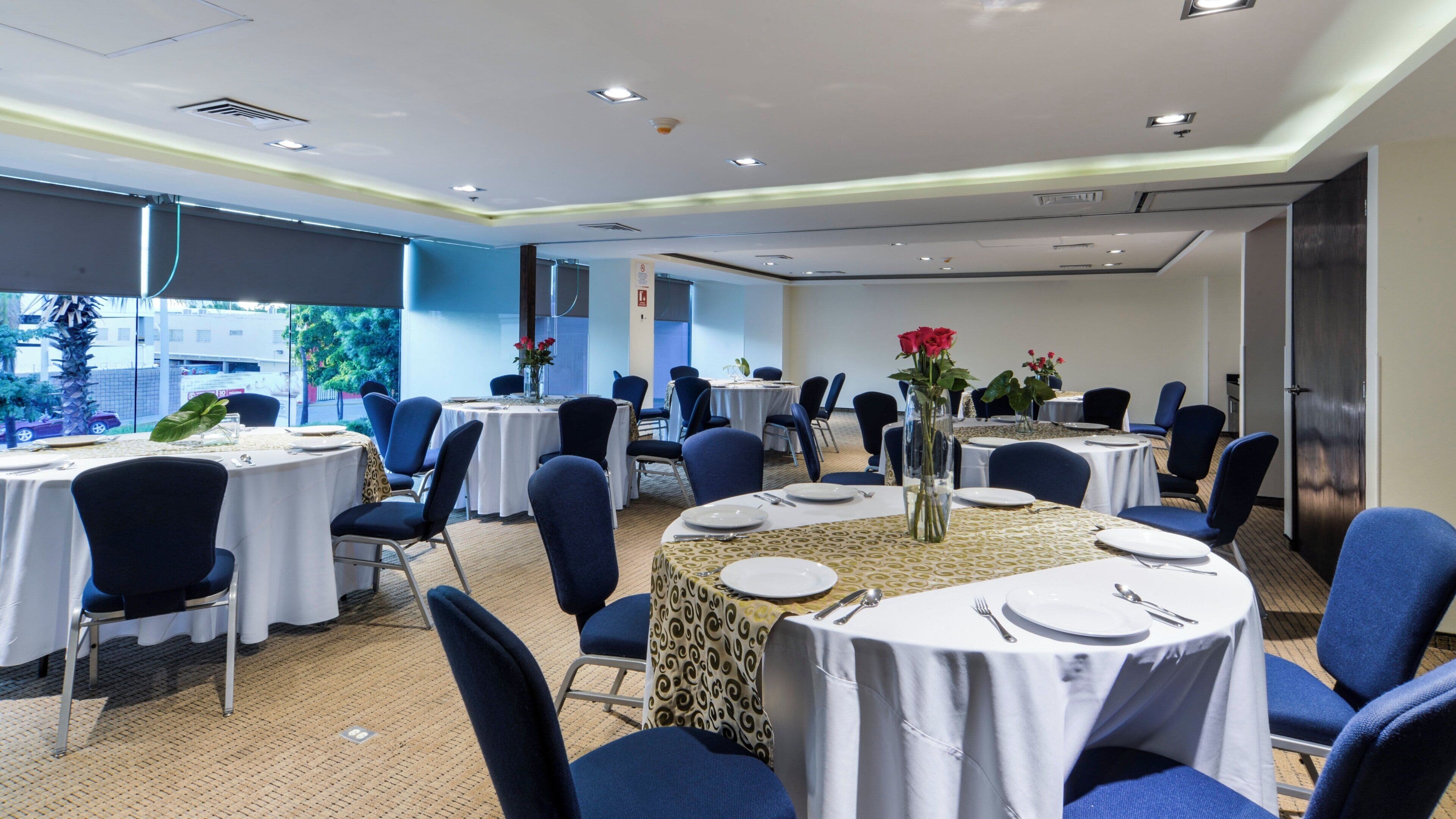 Un salón de conferencias con mesas redondas, sillas azules y manteles blancos.