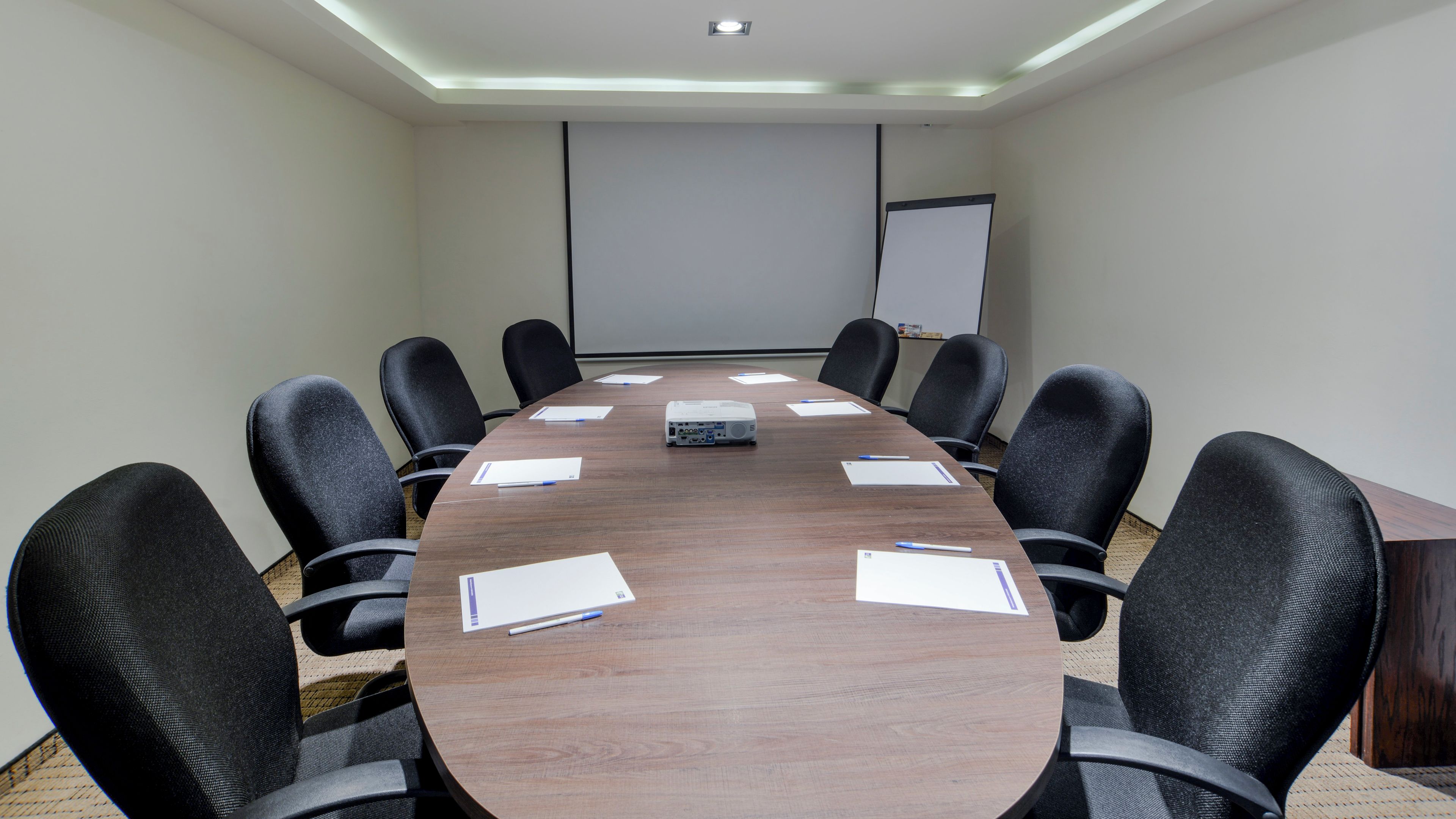 A conference room with a long table, black chairs, a projector, and a whiteboard.