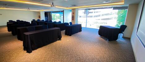 A conference room with tables and chairs, carpeted floor, and large windows.