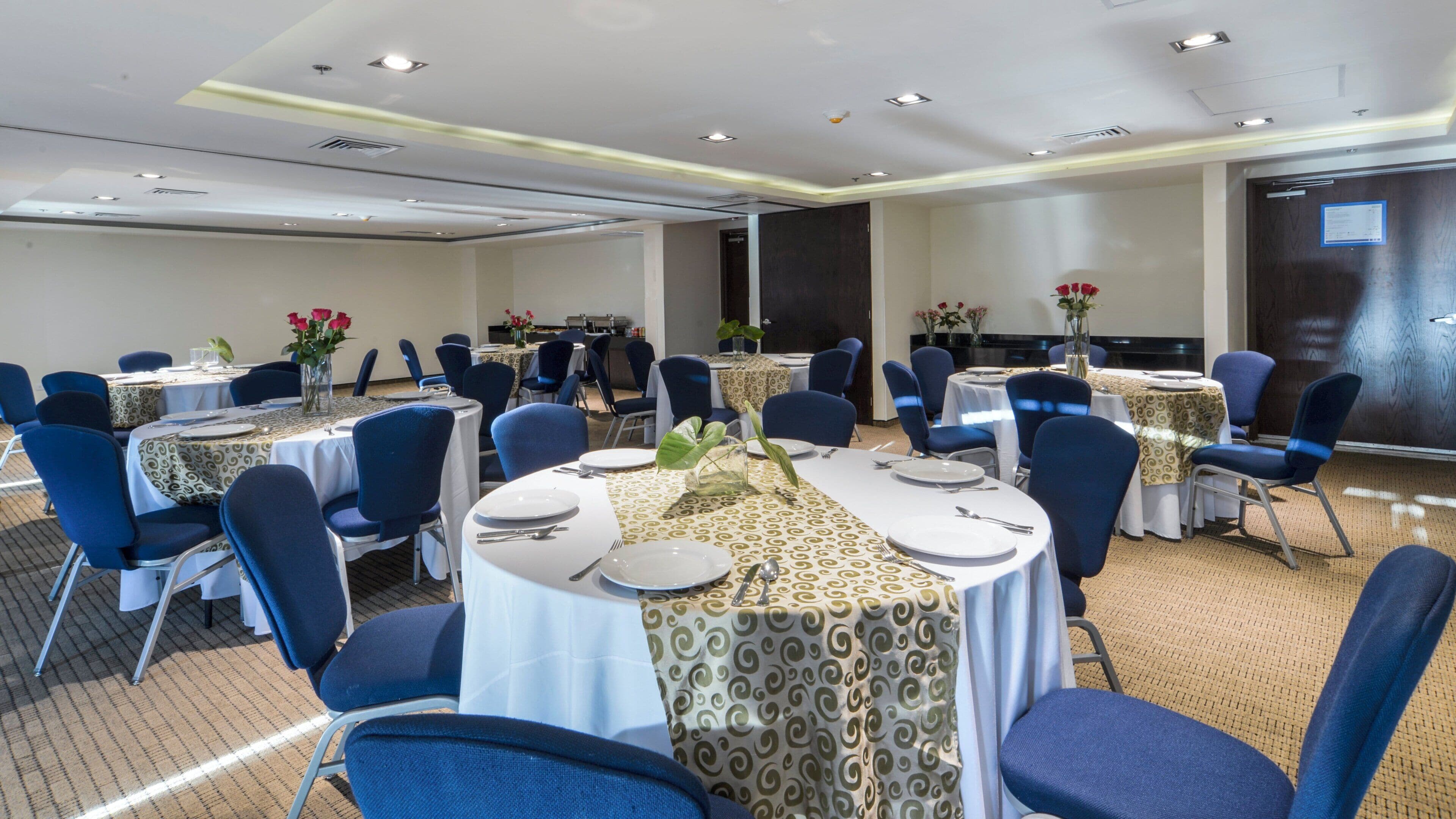 Un salón de conferencias con mesas redondas, sillas azules y manteles blancos.