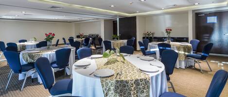 Un salón de conferencias con mesas redondas, sillas azules y manteles blancos.