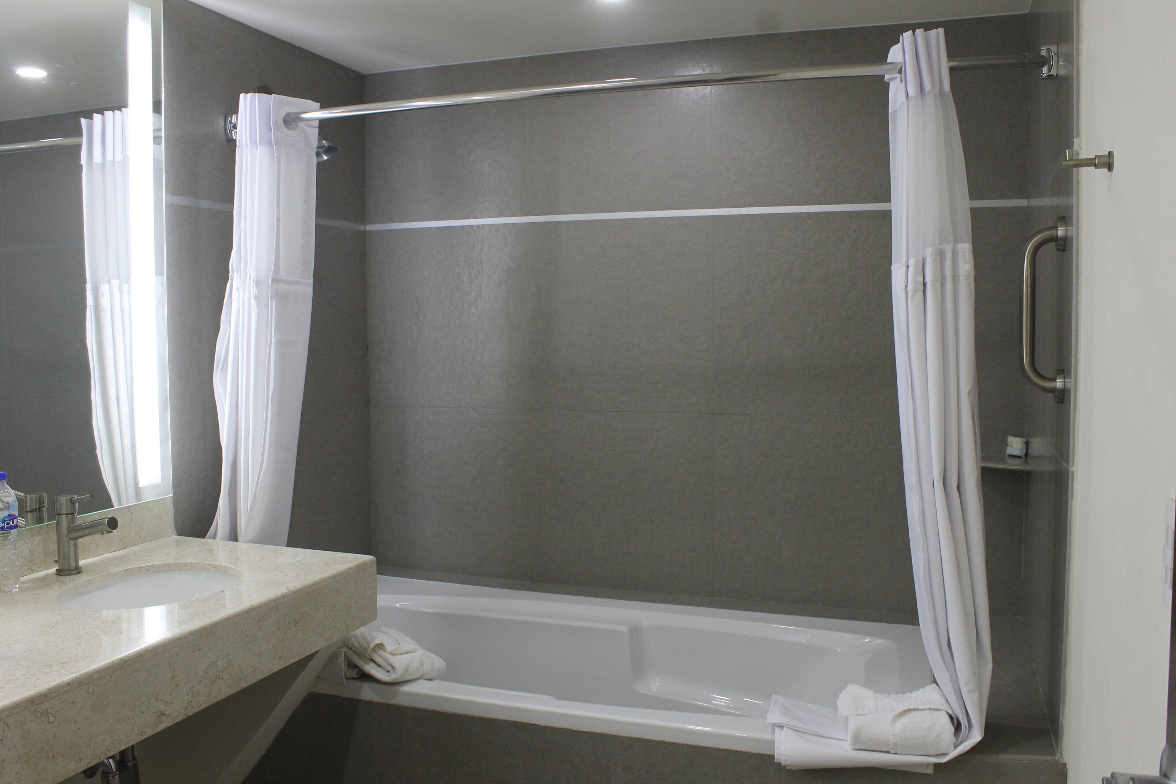 A modern bathroom with a bathtub, a shower curtain, a glass shower enclosure, and a sink with a faucet.