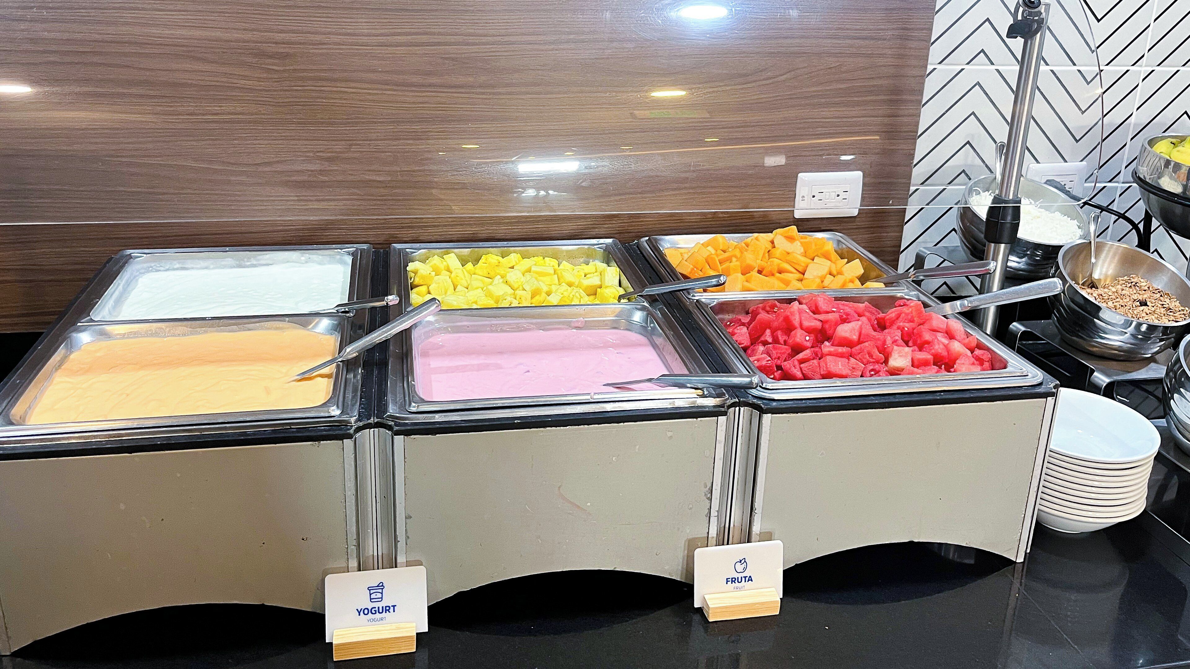 A buffet with multiple containers of yogurt and fruit.