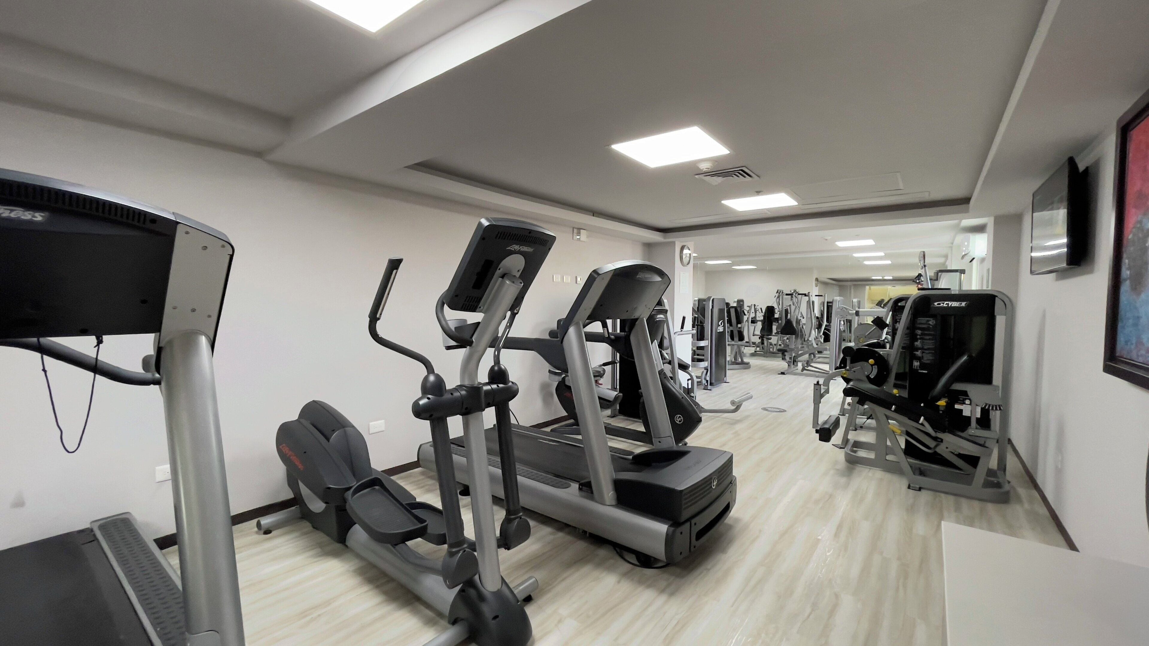 Un gimnasio con cintas de correr, elípticas y equipo de pesas.