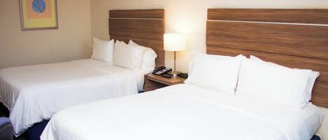 Una habitación de hotel con dos camas individuales, una mesita de noche con lámpara y un cuadro en la pared.