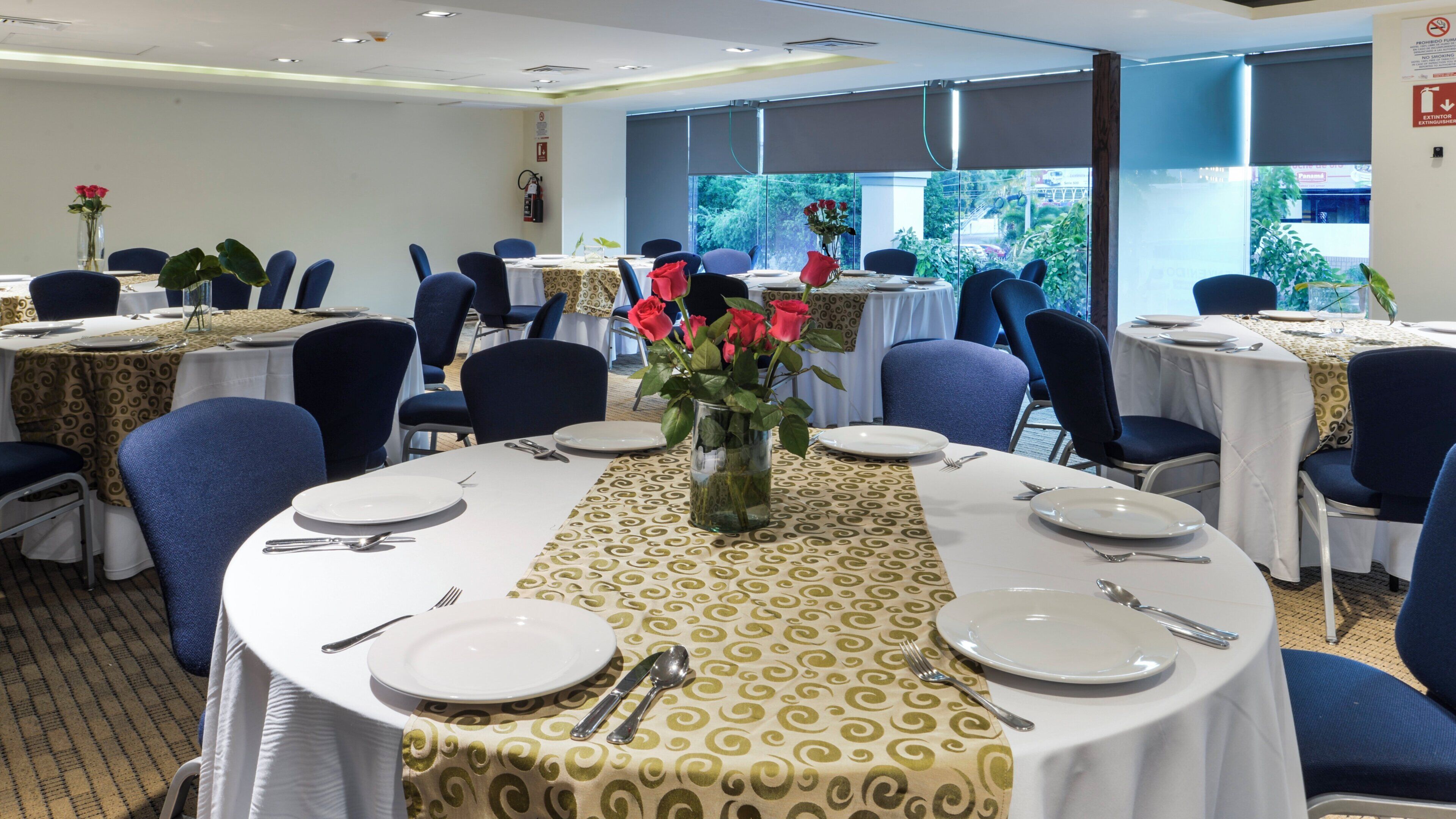 Un comedor con mesas redondas, sillas y centros de mesa con flores.