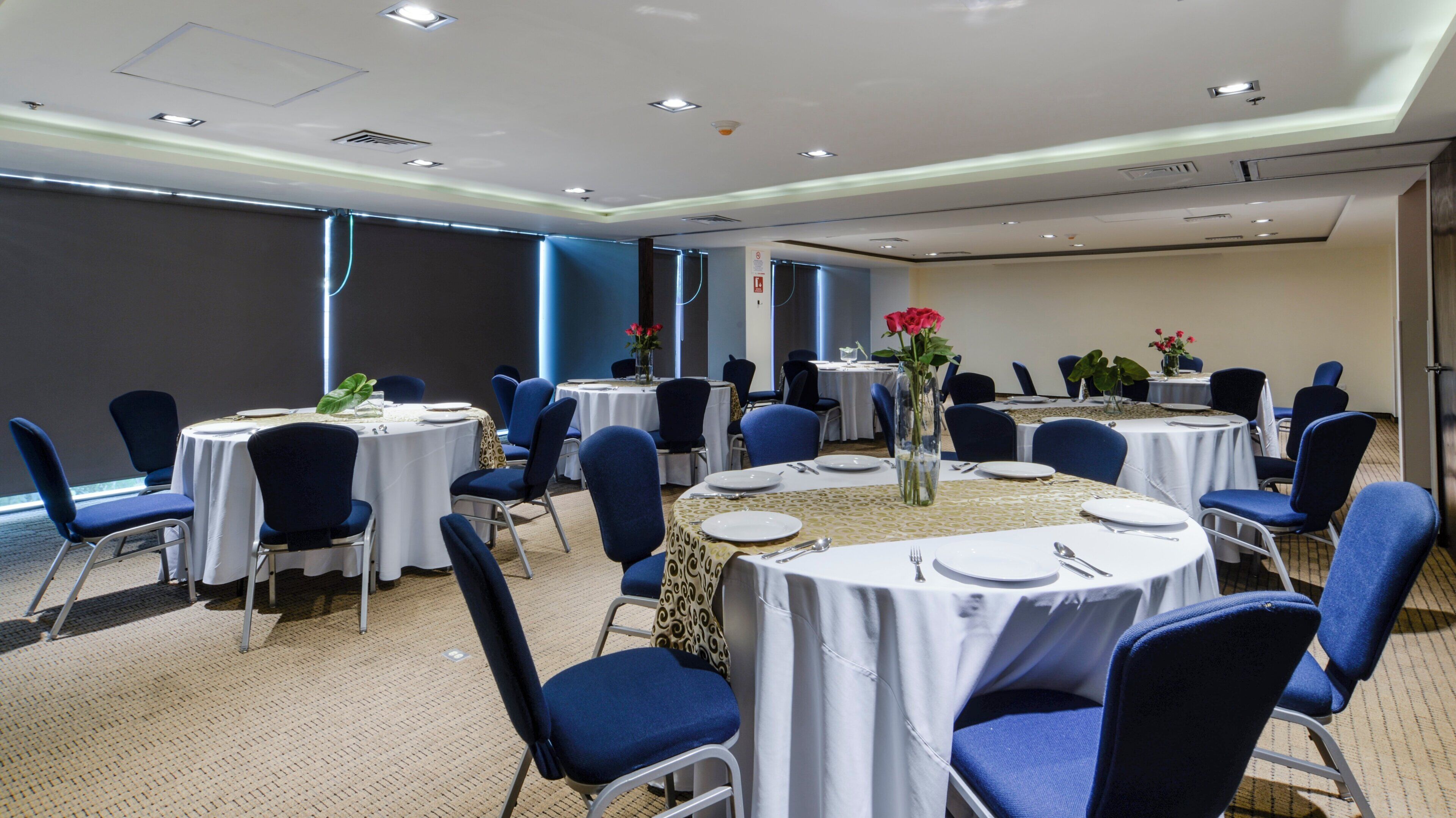 Un salón de conferencias con mesas redondas, sillas y centros de mesa con flores.