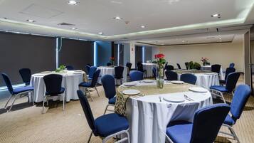 Un salón de conferencias con mesas redondas, sillas y centros de mesa con flores.