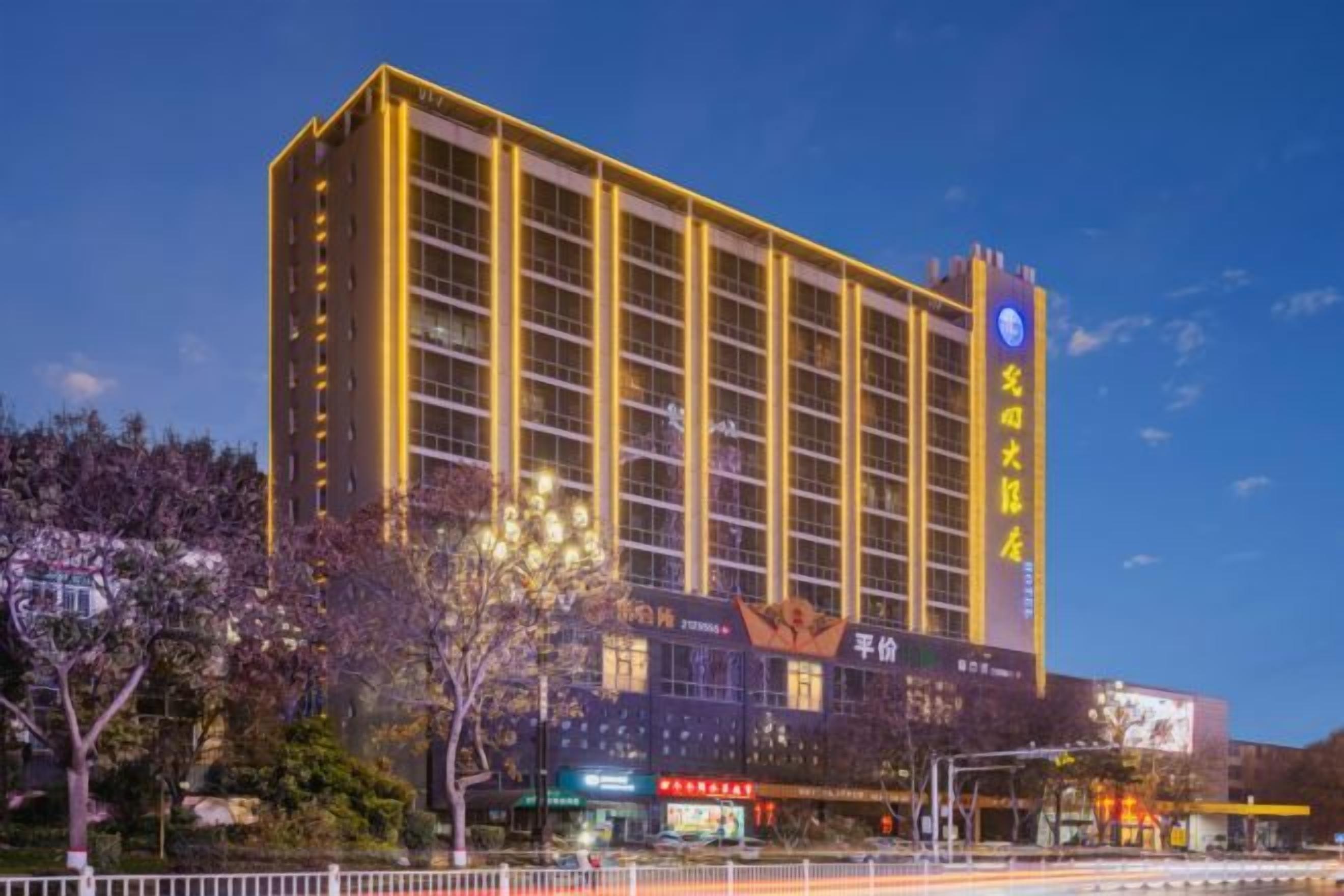 A multi-story hotel with a prominent sign, surrounded by trees and a clear sky.