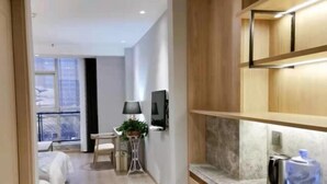 A modern hotel room with a wooden floor, a bed, a small table with a lamp, a TV mounted on the wall, and a water dispenser. - Guangming Hotel (Weinan)