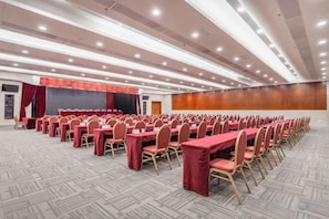 Una sala de conferències amb files de taules i cadires, un escenari i un sòl amb moqueta.