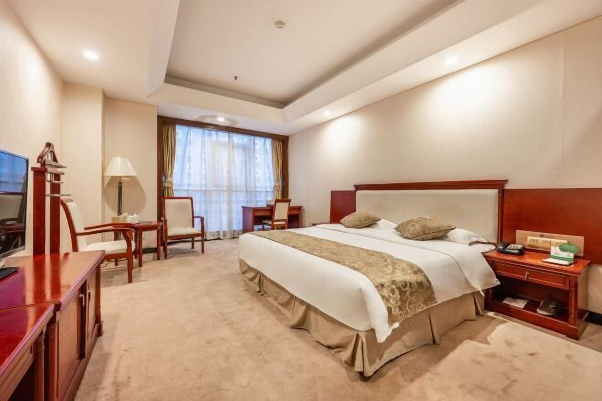Une chambre d’hôtel avec un grand lit, un bureau, une chaise, une lampe et un téléviseur.