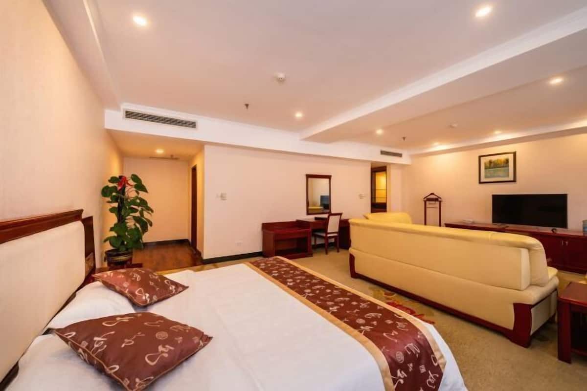 Quarto de hotel com cama, sofá, escrivaninha e televisão.
