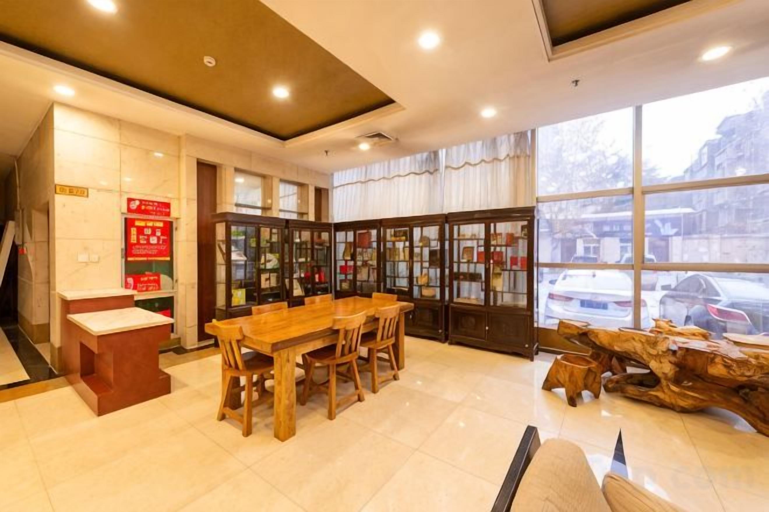 A hotel lobby with a reception desk, a wooden dining table, and a large window with a view of the street.