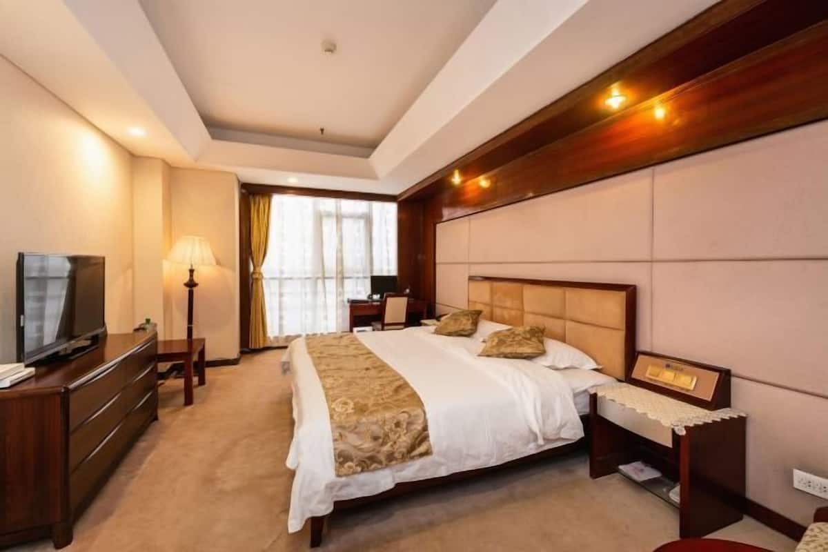 Quarto de hotel com cama, mesa de cabeceira, luminária, televisão e escrivaninha com cadeira.