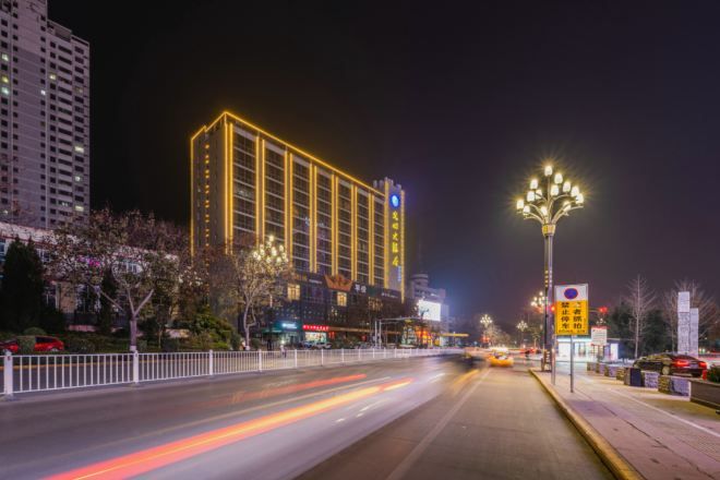 A brightly lit hotel with a modern facade, a well-maintained sidewalk, and a clear road in the foreground.