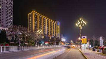 A brightly lit hotel with a modern facade, a well-maintained sidewalk, and a clear road in the foreground.