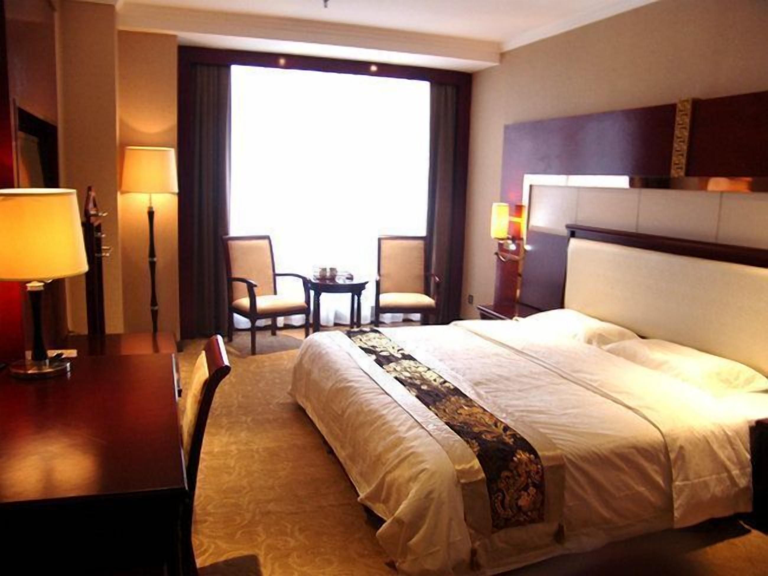 Hotellihuone, jossa on suuri sänky, kaksi tuolia, pieni pöytä ja työpöytä, jossa on lamput.