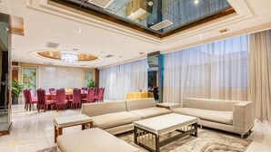 A spacious living area with a large sofa, ottoman, and coffee table, a dining area with red chairs, and a high ceiling with a skylight. - Guangming Hotel (Weinan)
