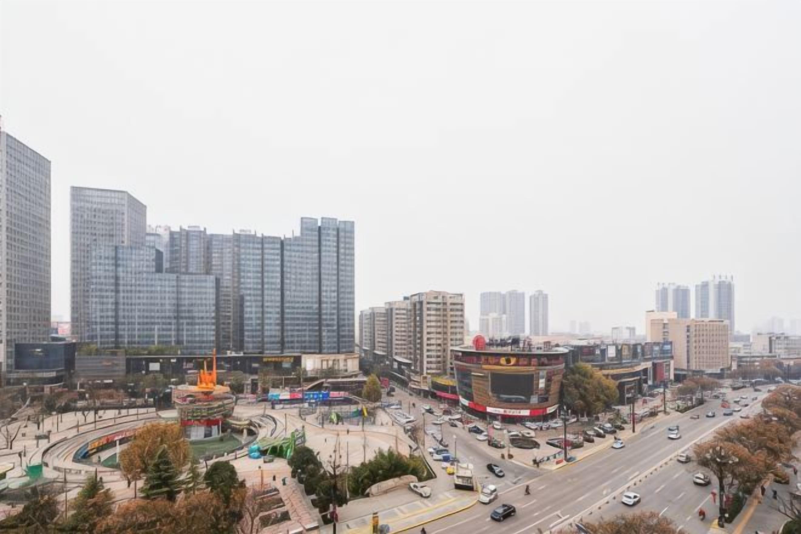 Paisagem urbana com edifícios altos, um rotatório e uma rua movimentada.