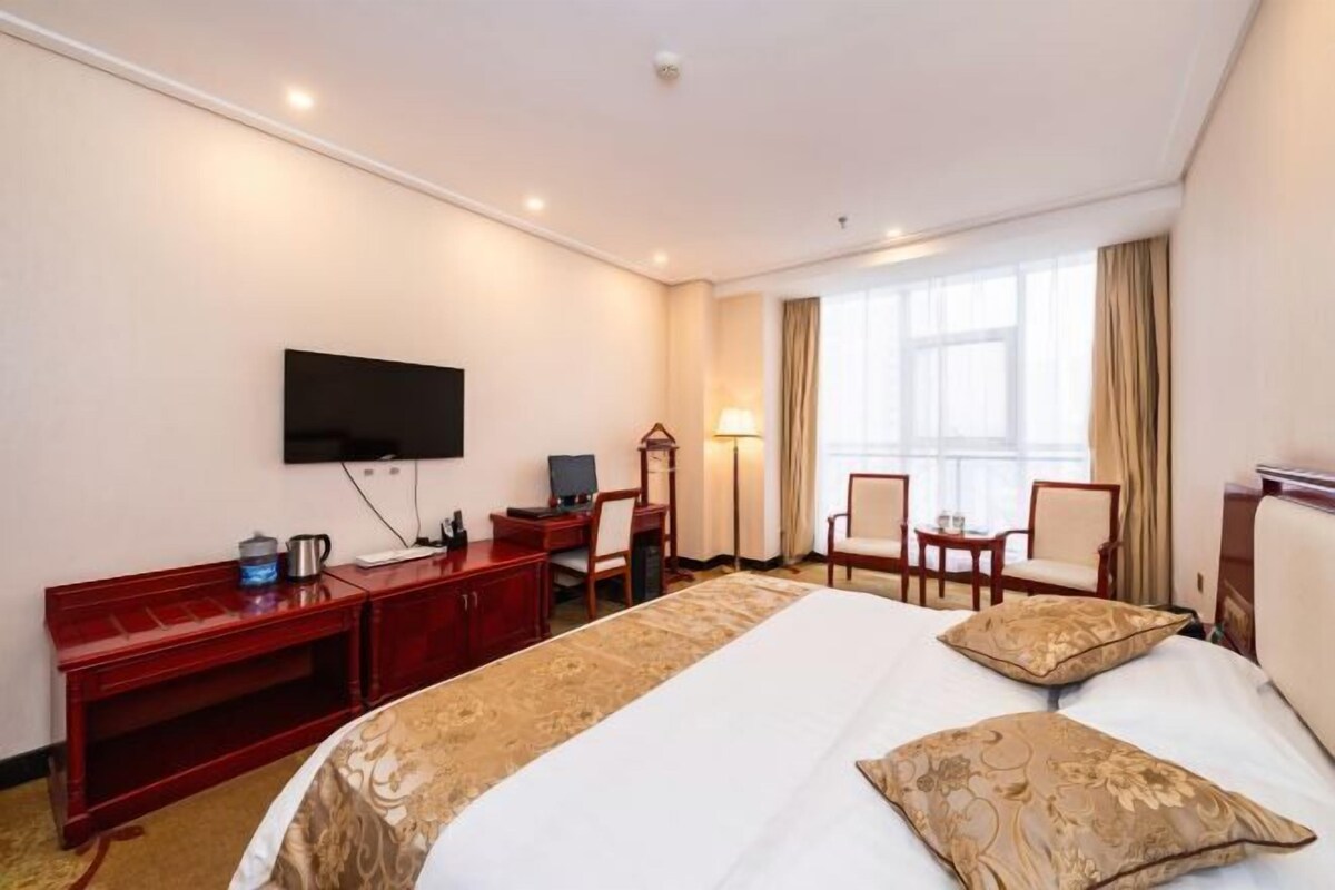 Une chambre d’hôtel avec un grand lit, un bureau avec un ordinateur, un téléviseur fixé au mur et une fenêtre avec des rideaux.