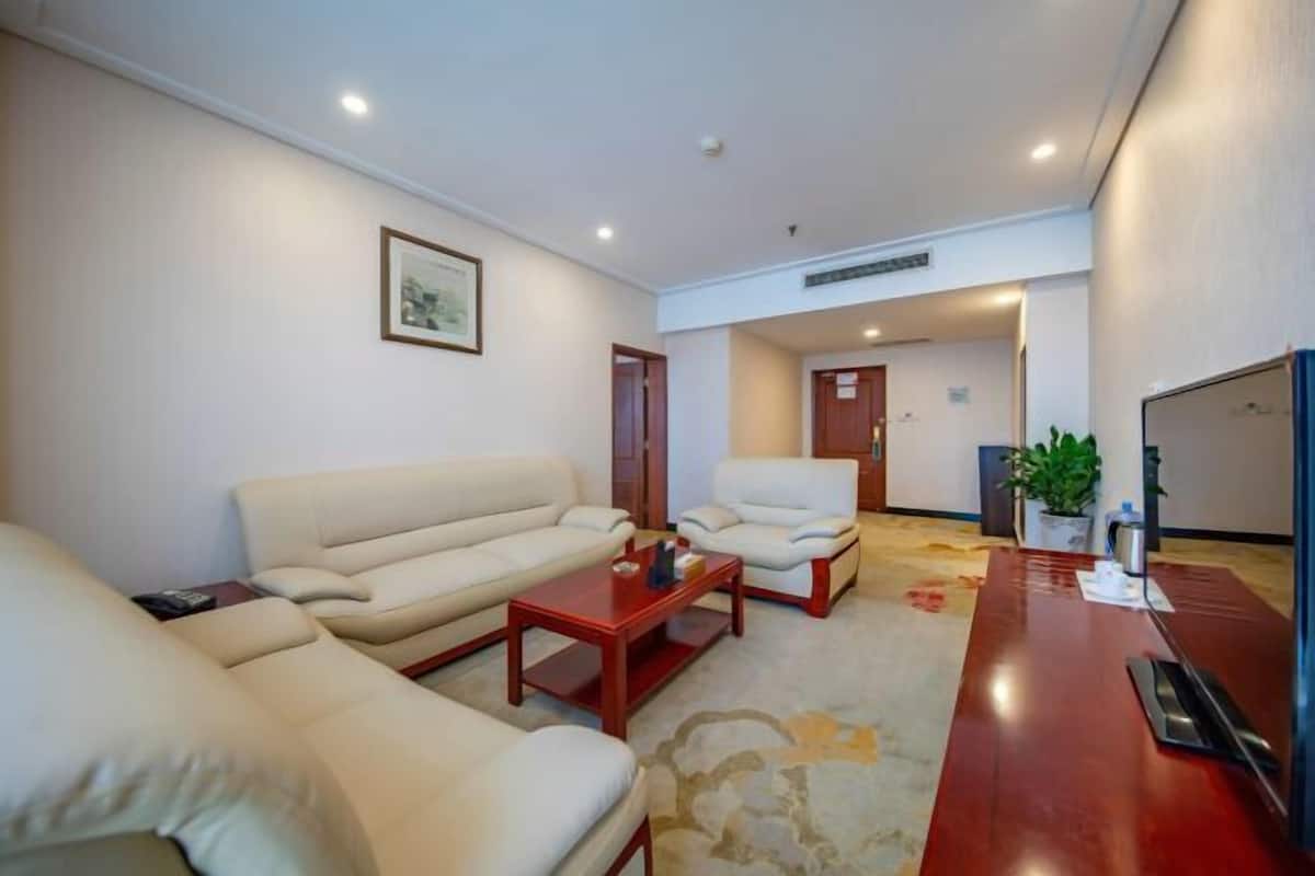 Sala de estar com sofá, poltrona e mesa de centro. Há uma planta e uma televisão à direita.