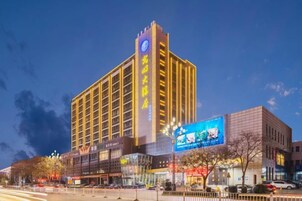 Un hotel de varios pisos con un letrero llamativo, situado en una calle urbana con otros edificios y comercios.