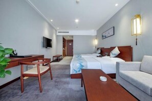 Une chambre d’hôtel équipée d’un lit, d’un bureau, d’une chaise, d’un canapé et d’un téléviseur fixé au mur.