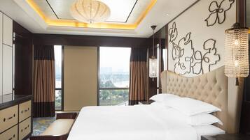 A hotel room with a large bed, a view of a cityscape, a chandelier, and a decorative wall piece.