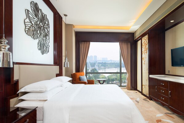 A hotel room with a large bed, a TV, a chair, and a window with a city view. - Sheraton Changde Wuling Hotel (Changde)