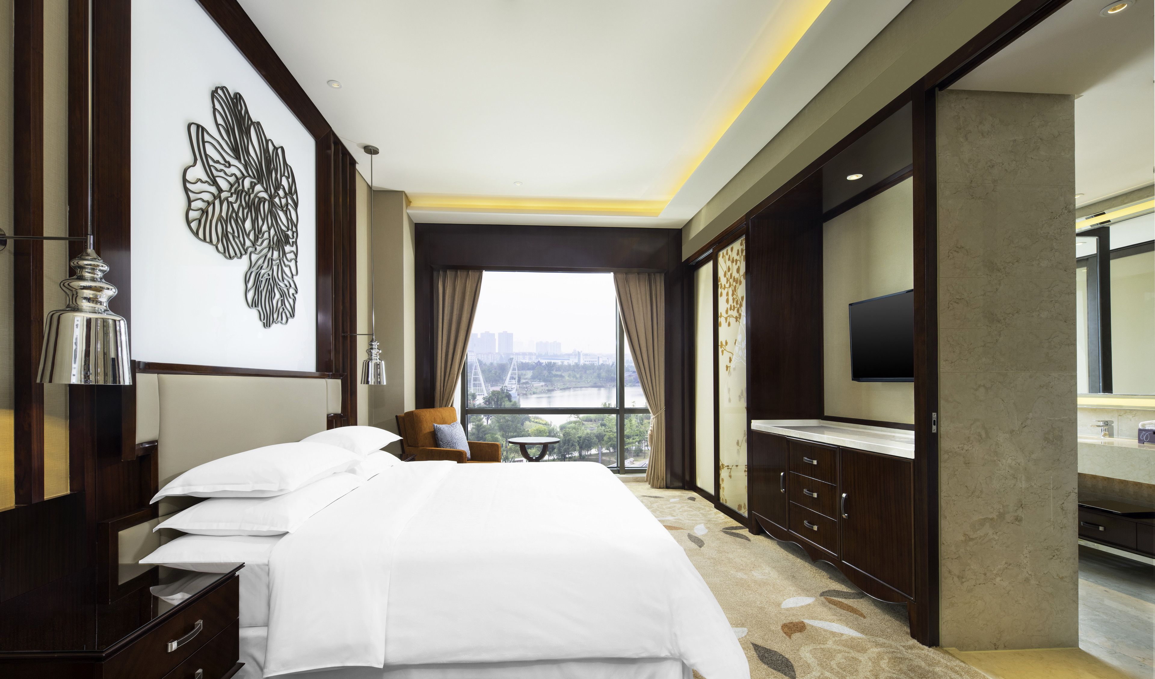 Habitación de hotel con una cama grande, televisión, vista panorámica de la ciudad y un adorno de pared.