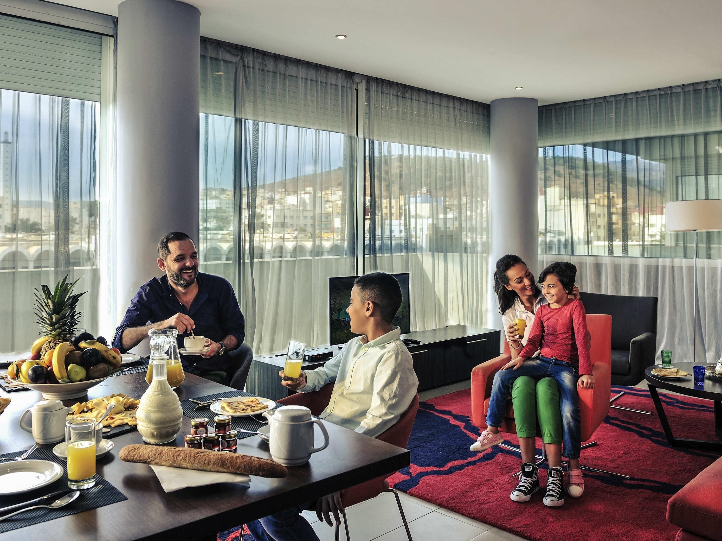 A family dining at a table with breakfast items, a city view, and a modern interior.