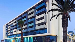 A modern multi-story hotel with a prominent blue and white facade, large windows, and a well-maintained outdoor area with palm trees. - Hotel Mercure Rif Nador (Nador)