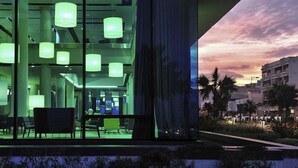 A modern building with large windows, multiple green cylindrical lights, and a view of palm trees and a sunset. - Hotel Mercure Rif Nador (Nador)