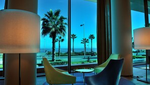 A modern hotel lobby with large windows, a palm tree view, and contemporary furniture. - Hotel Mercure Rif Nador (Nador)