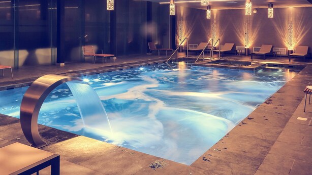A modern indoor pool with a clear water feature, lounge chairs, and ambient lighting. - Hotel Mercure Rif Nador (Nador)