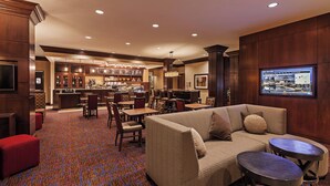 A hotel lobby with a bar area, seating arrangements, and a large screen displaying information.
