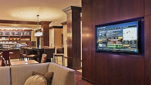 A hotel lobby with a bar area, seating, and a digital screen displaying news.
