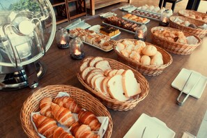A buffet table with various baked goods, including bread, pastries, and desserts. - Pousada Águas Claras (Búzios)