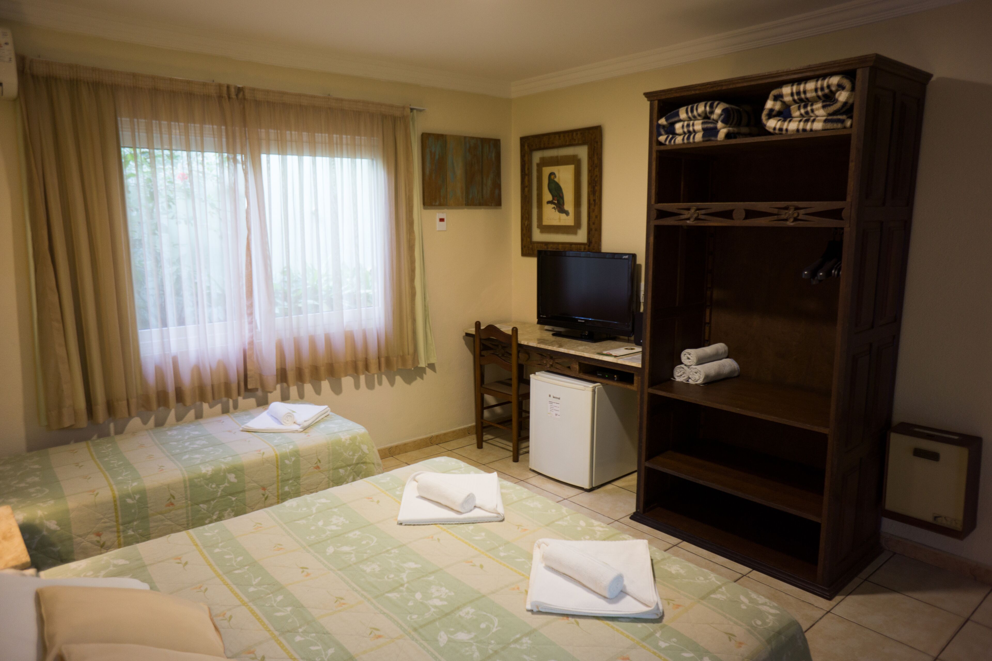 A hotel room with two beds, a desk with a computer, a television, and a wardrobe.