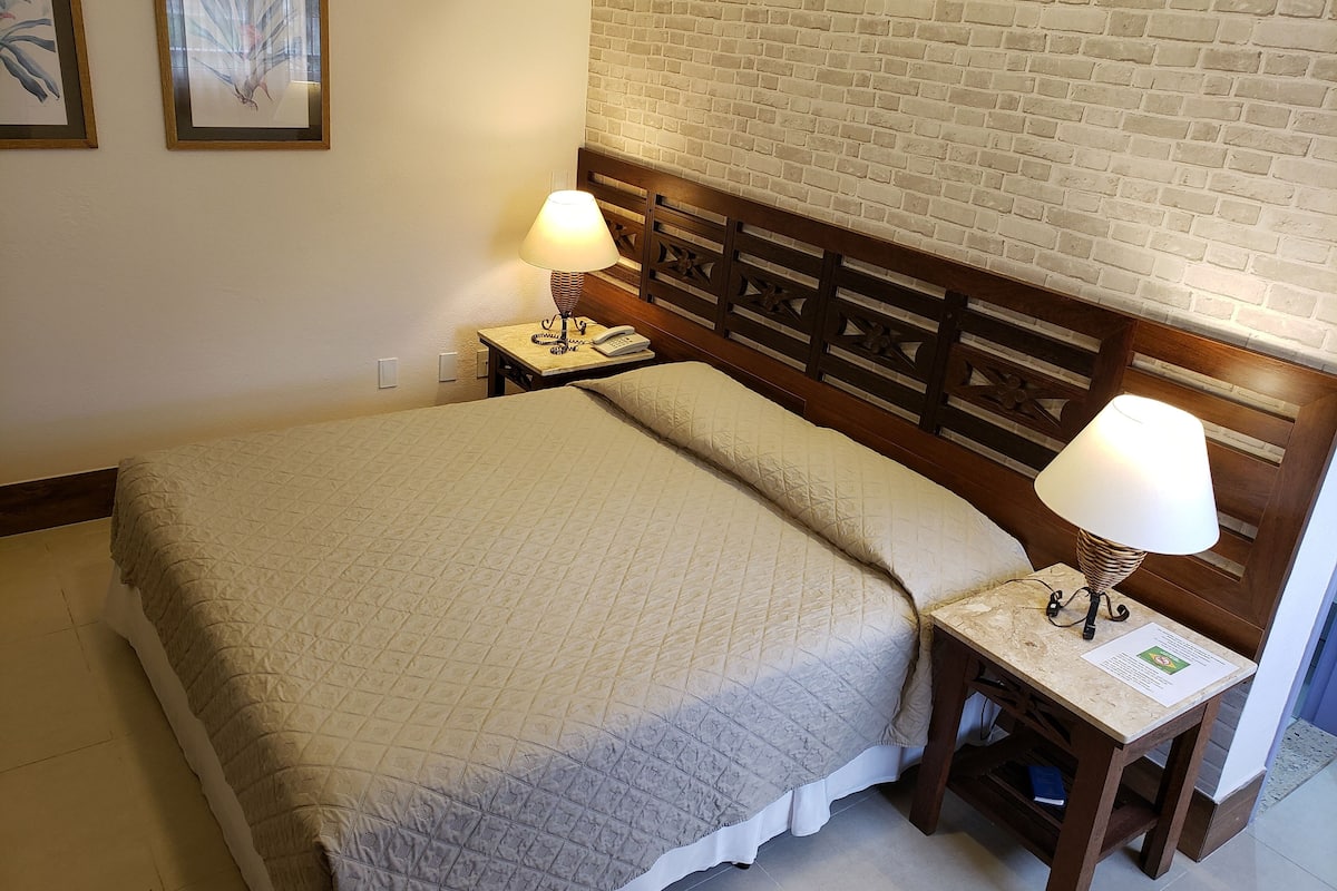 Una cama bien hecha con un edredón acolchado, dos lámparas de noche y un cabecero de madera frente a una pared de ladrillo.