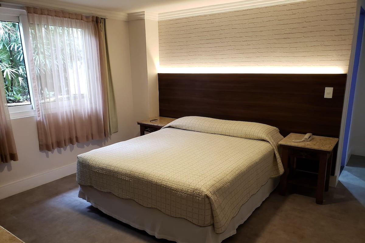 Una cama bien hecha con una colcha acolchada, un cabecero de madera y una mesita de noche con un teléfono.