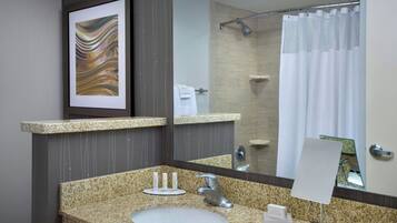 Un baño con encimera de granito, un lavamanos, un espejo, una obra de arte enmarcada y una cortina de ducha.