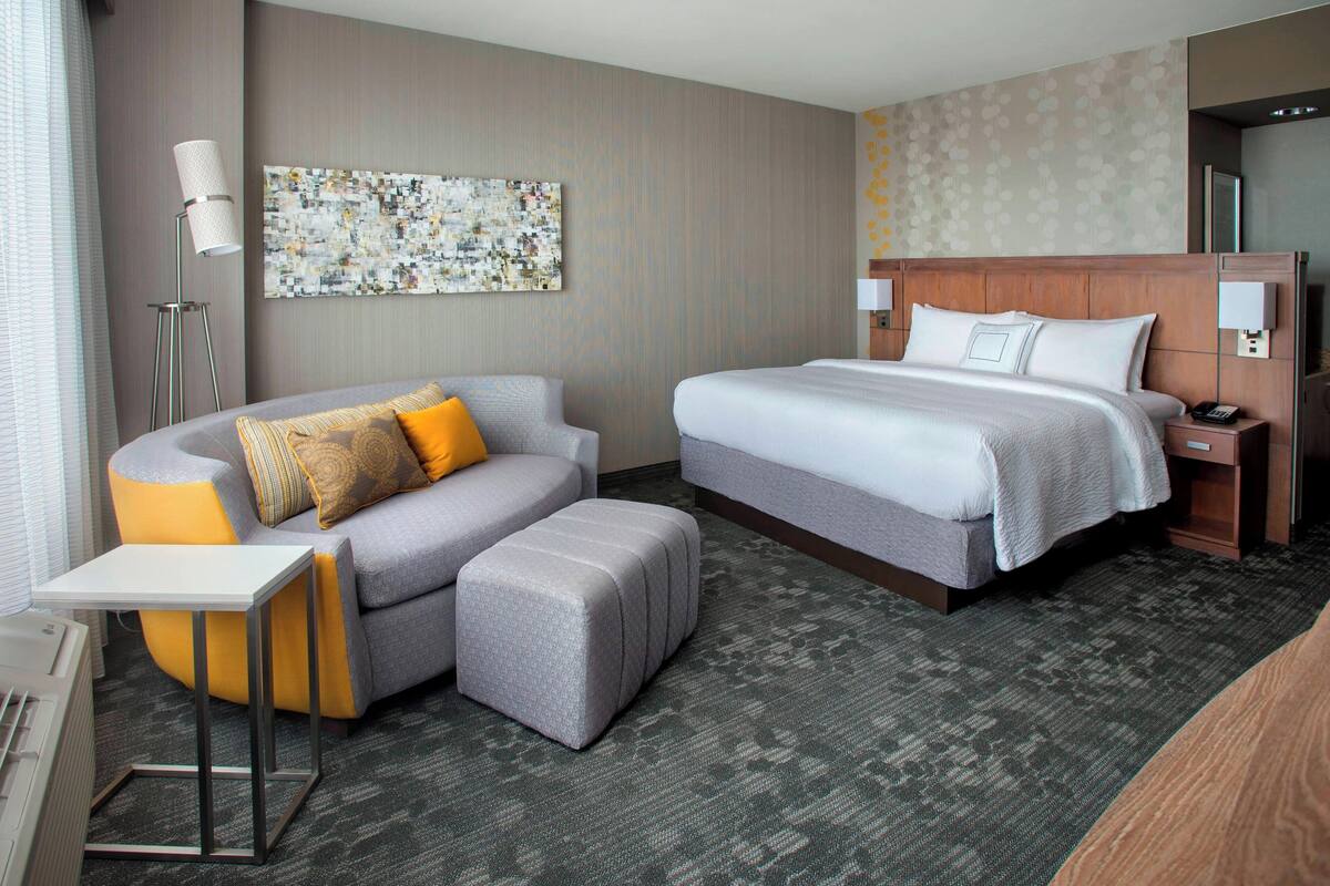 A hotel room with a bed, a sofa, a small table, and a floor lamp.