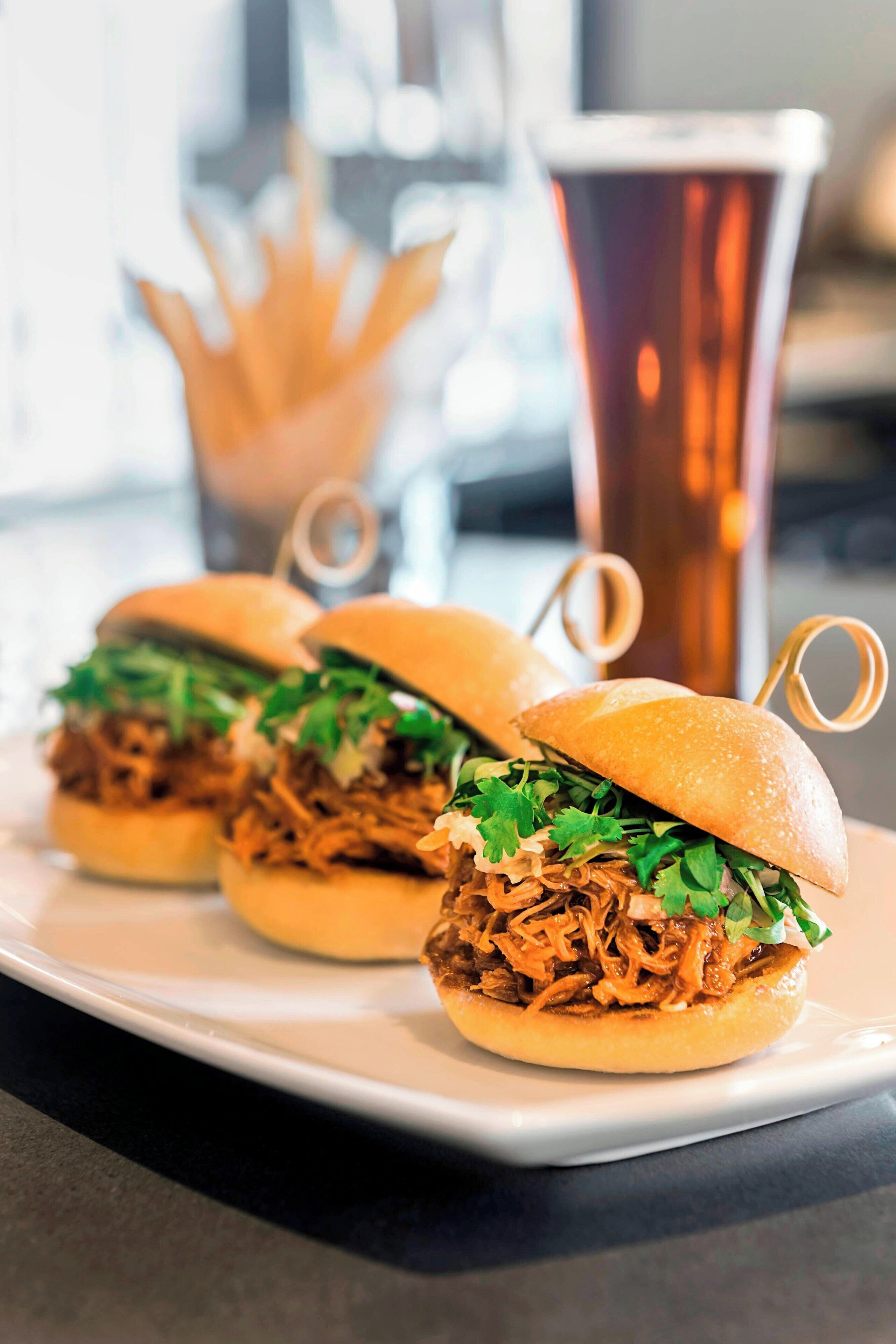 Three pulled pork sandwiches on a white plate with a copper mug in the background.