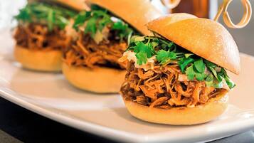 Three pulled pork sandwiches on a white plate with a copper mug in the background.