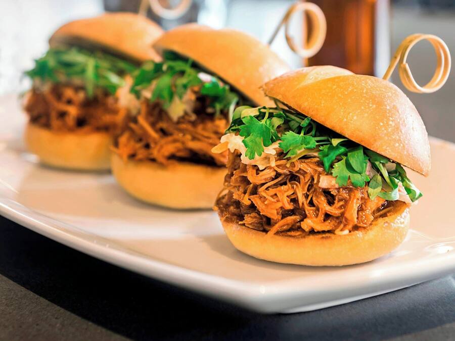Three pulled pork sandwiches on a white plate with a copper mug in the background.