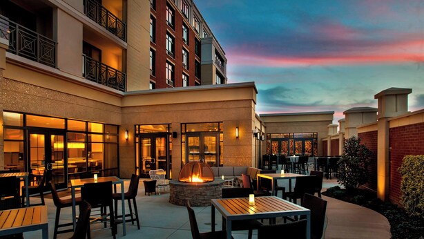 An outdoor patio area with tables and chairs, a fire pit, and a view of a building with balconies. - Courtyard by Marriott Philadelphia Lansdale (Harleysville)