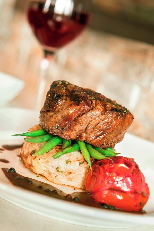 A plate with a steak, green beans, and a red vegetable, possibly a bell pepper, on a white plate.