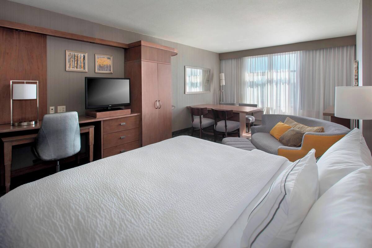 A hotel room with a large bed, a desk with a TV, a chair, a sofa, and a window with curtains.